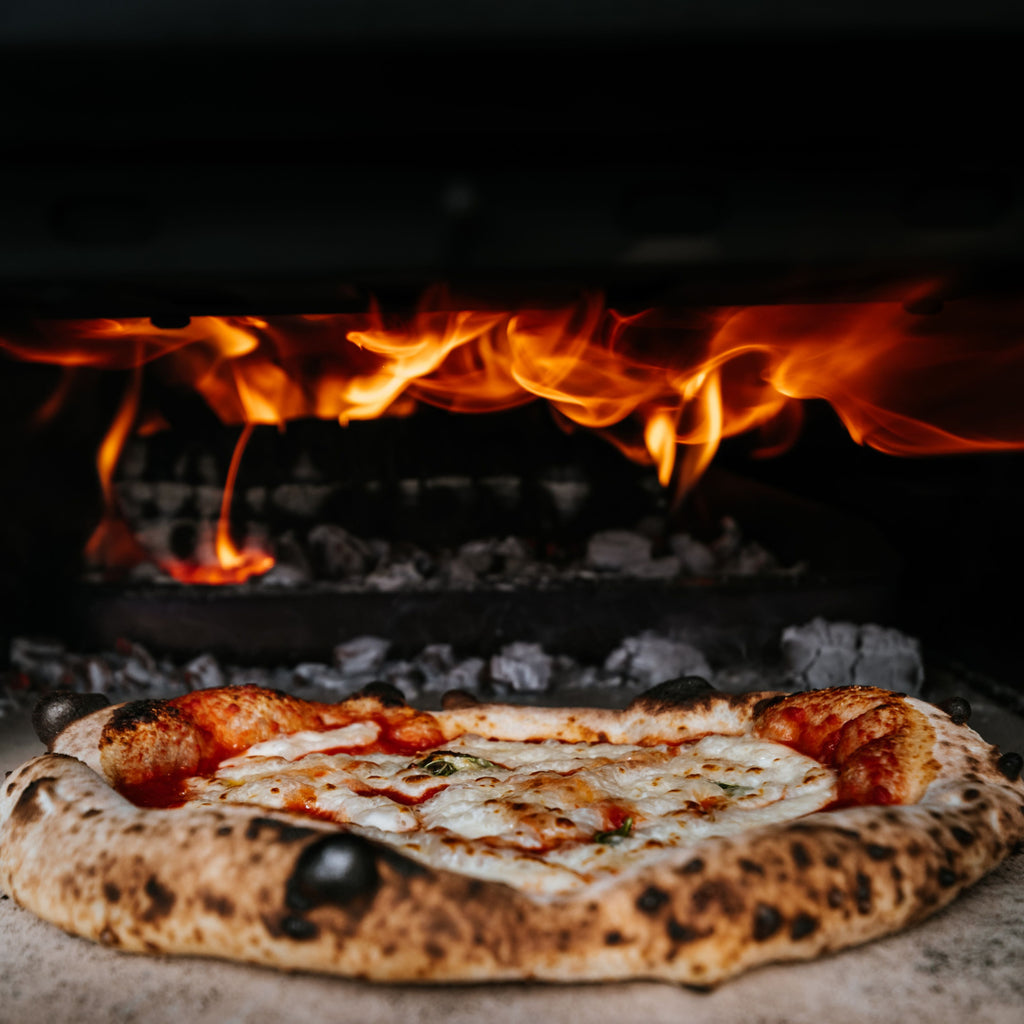 Pizza fotografiată în cuptorul pe lemne cu flacără aprinsă